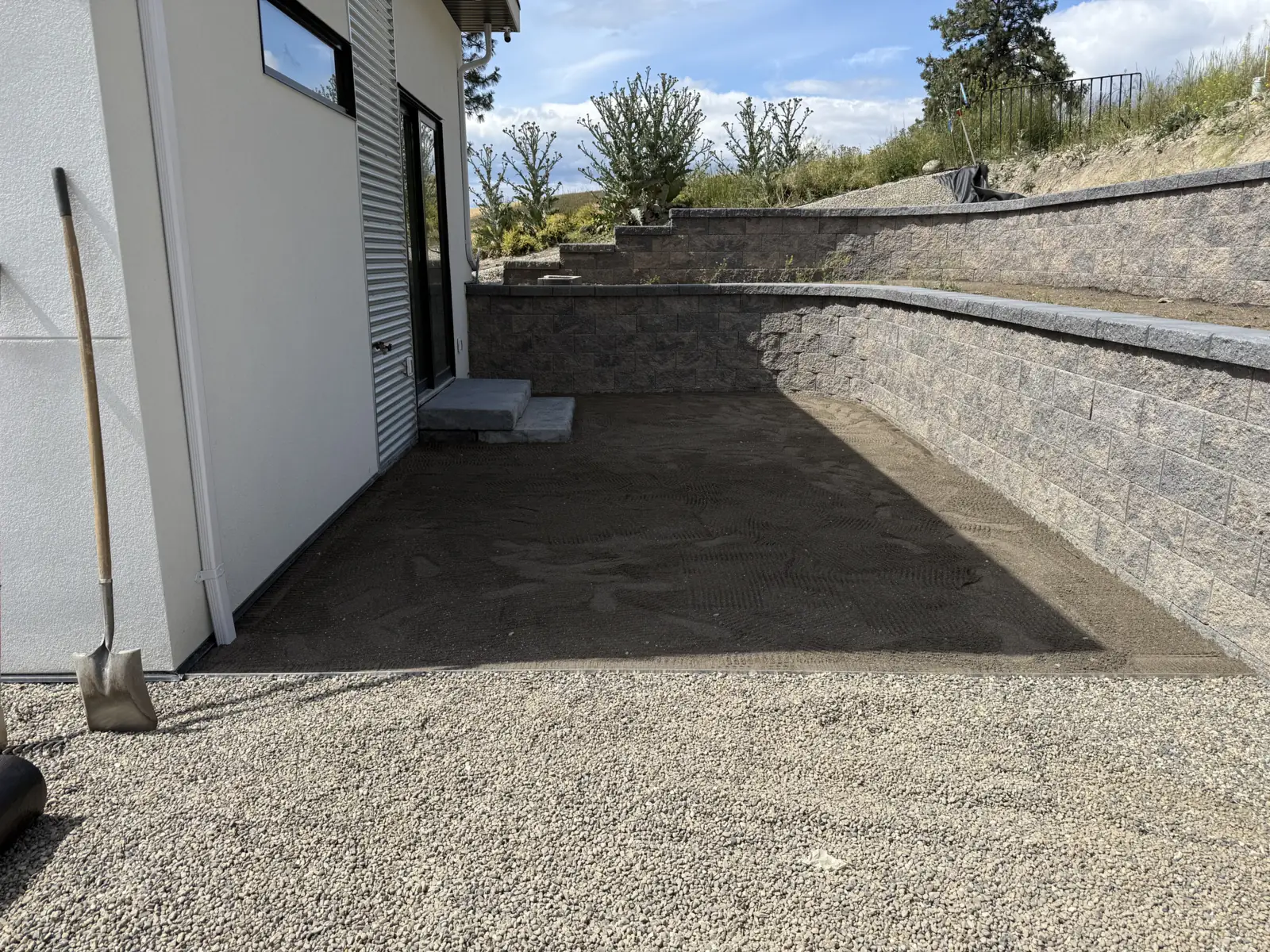 Paved courtyard between the house and a curved block retaining wall