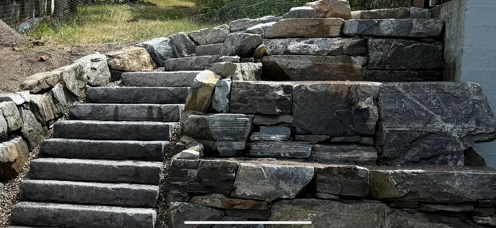 Stacked stone wall and stair run finished across a sloped yard