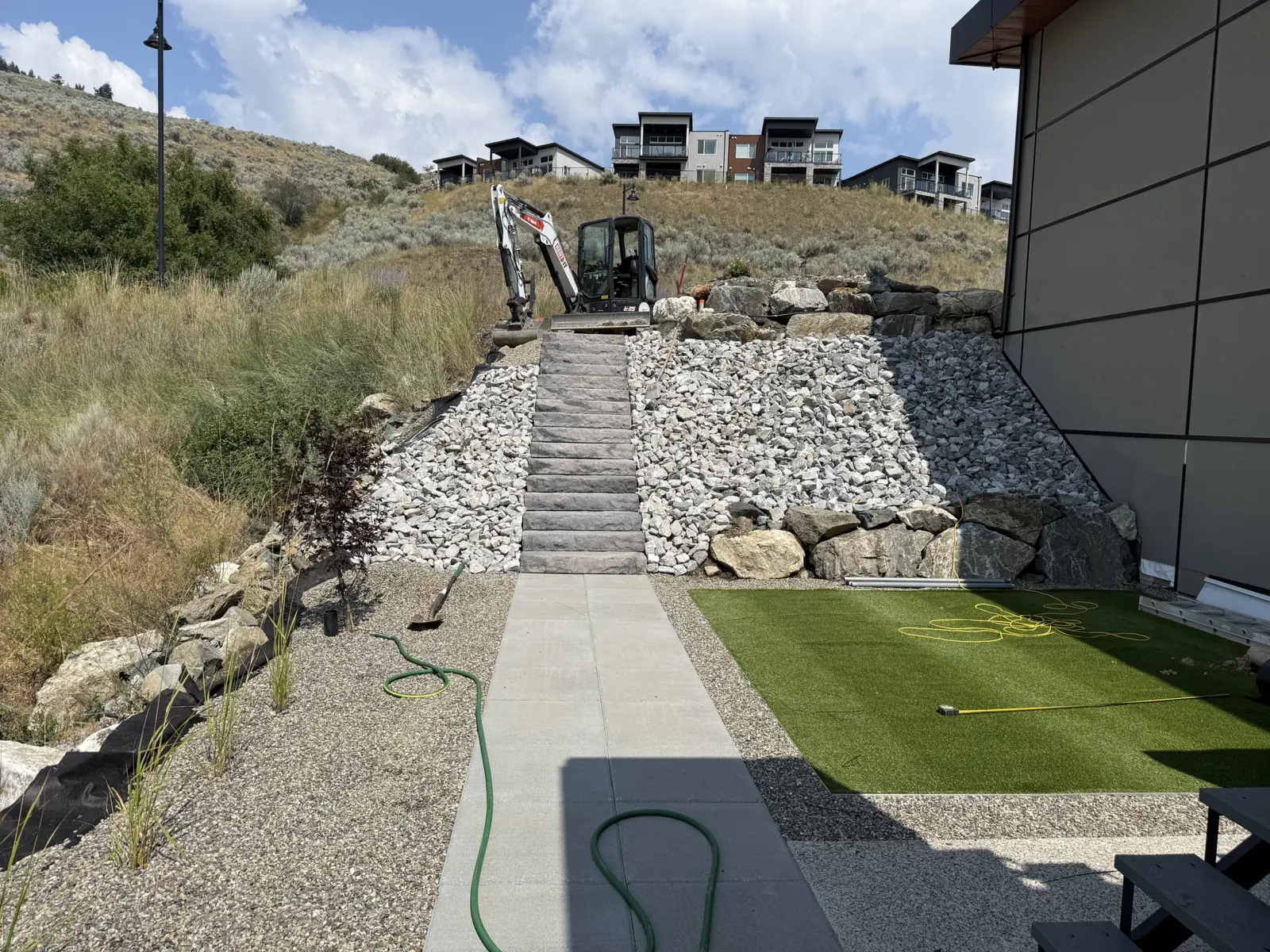Slab steps, turf and rock beds climbing the hill behind a modern home