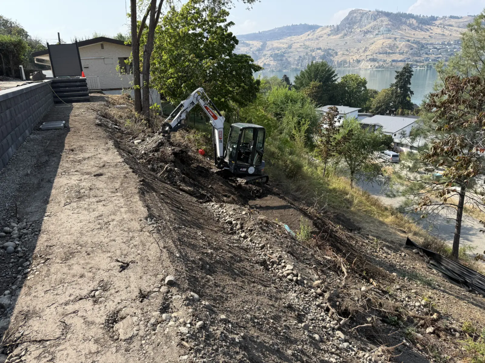 Mini excavator clearing the hillside beside a new block wall