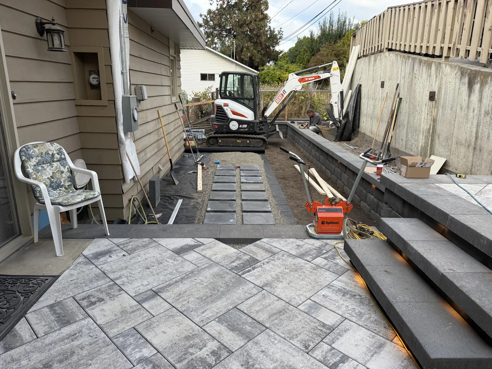 Paver patio and lit steps with the side yard excavated behind