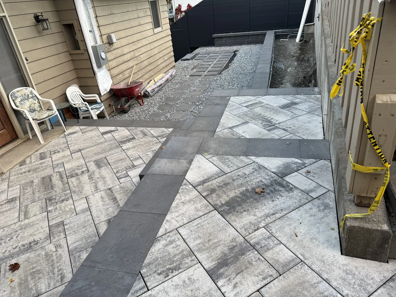 Paver patio with a dark border band running up the side of the house