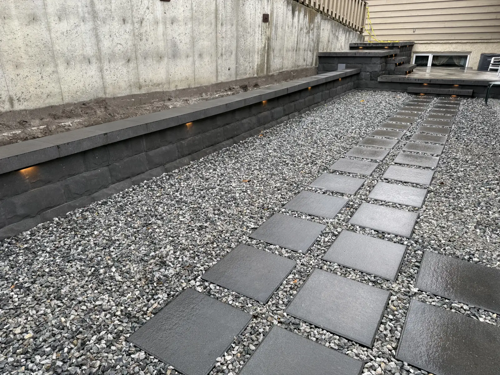 Dark slab stepping stones set in gravel along a lit block wall