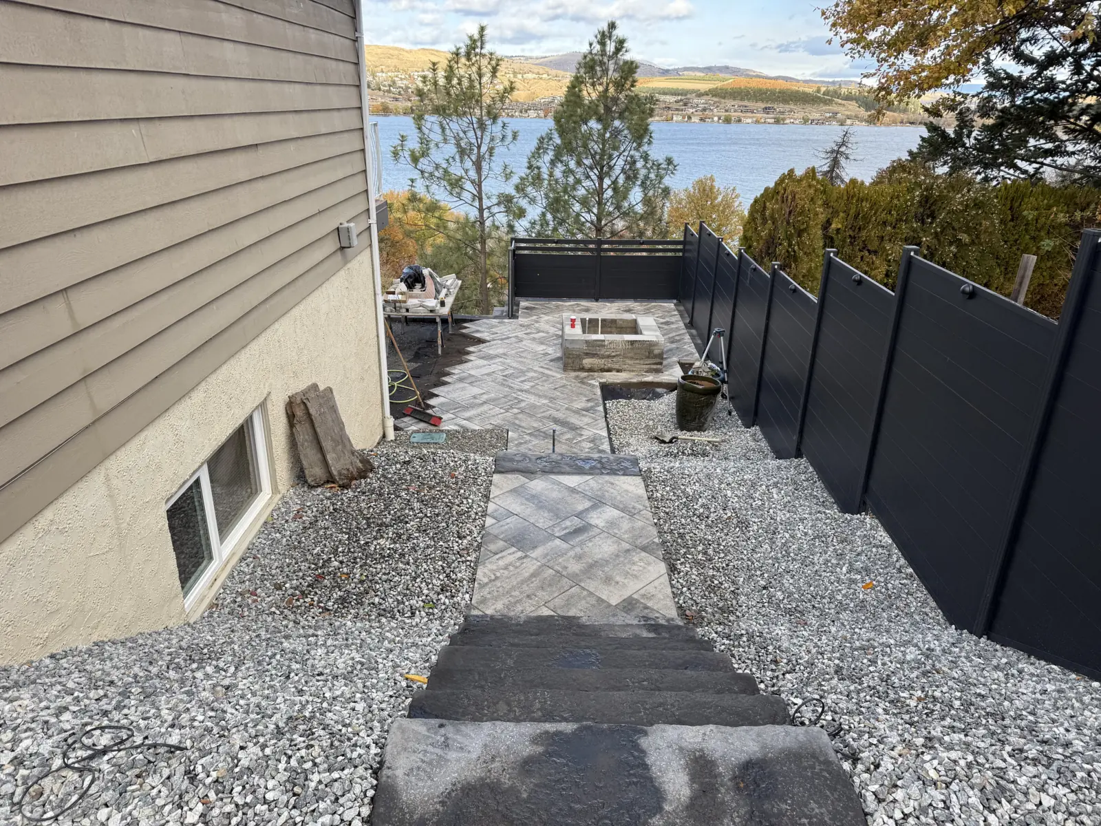 Stairs down to the patio between gravel beds and black privacy fencing, lake beyond