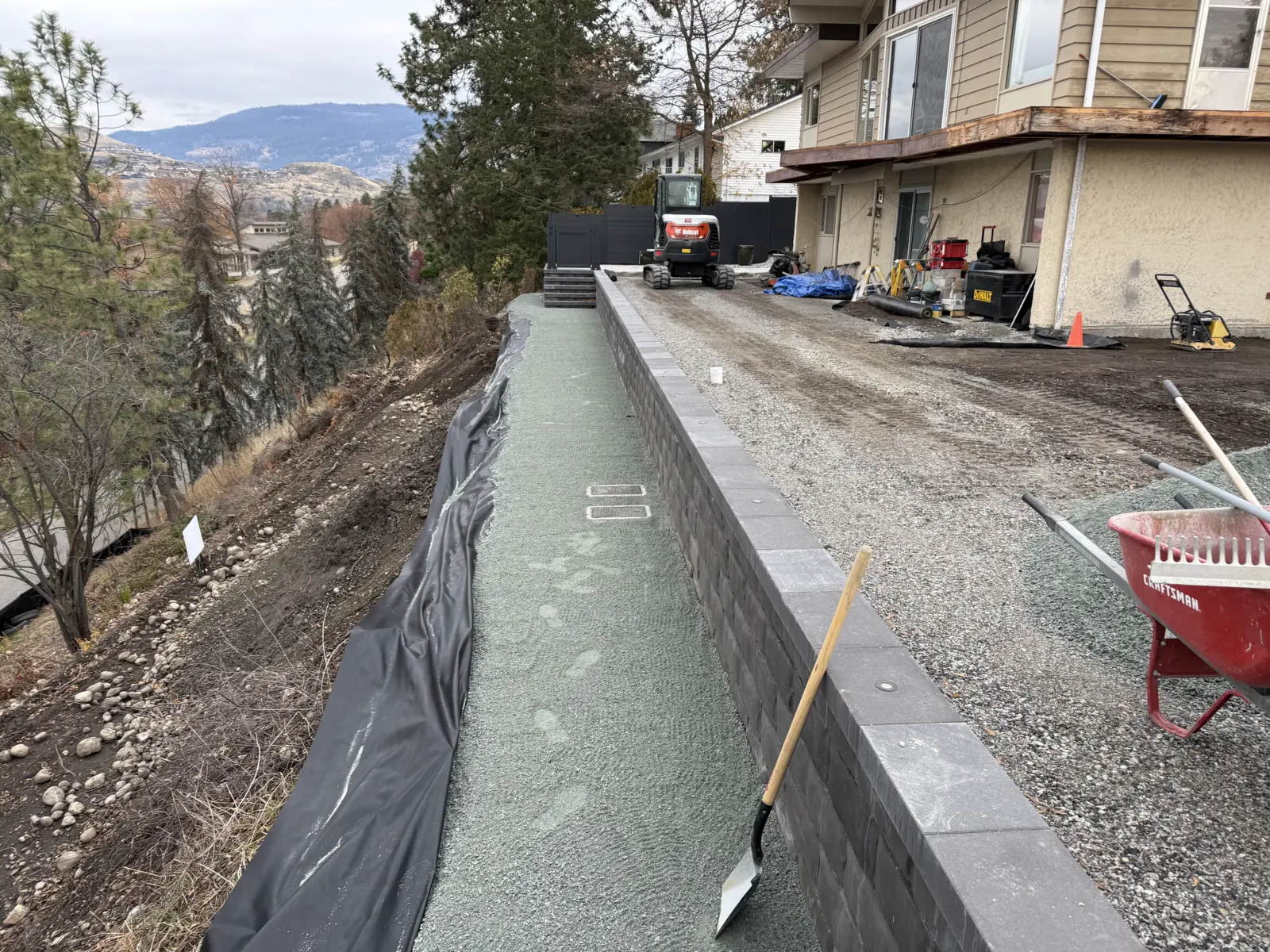Capped retaining wall with drain rock and filter fabric behind it on a slope