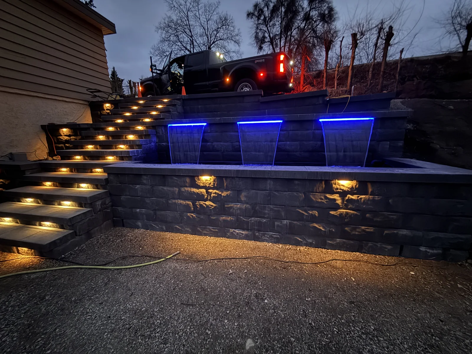 Lit stairs and blue water features across the terraced wall at night