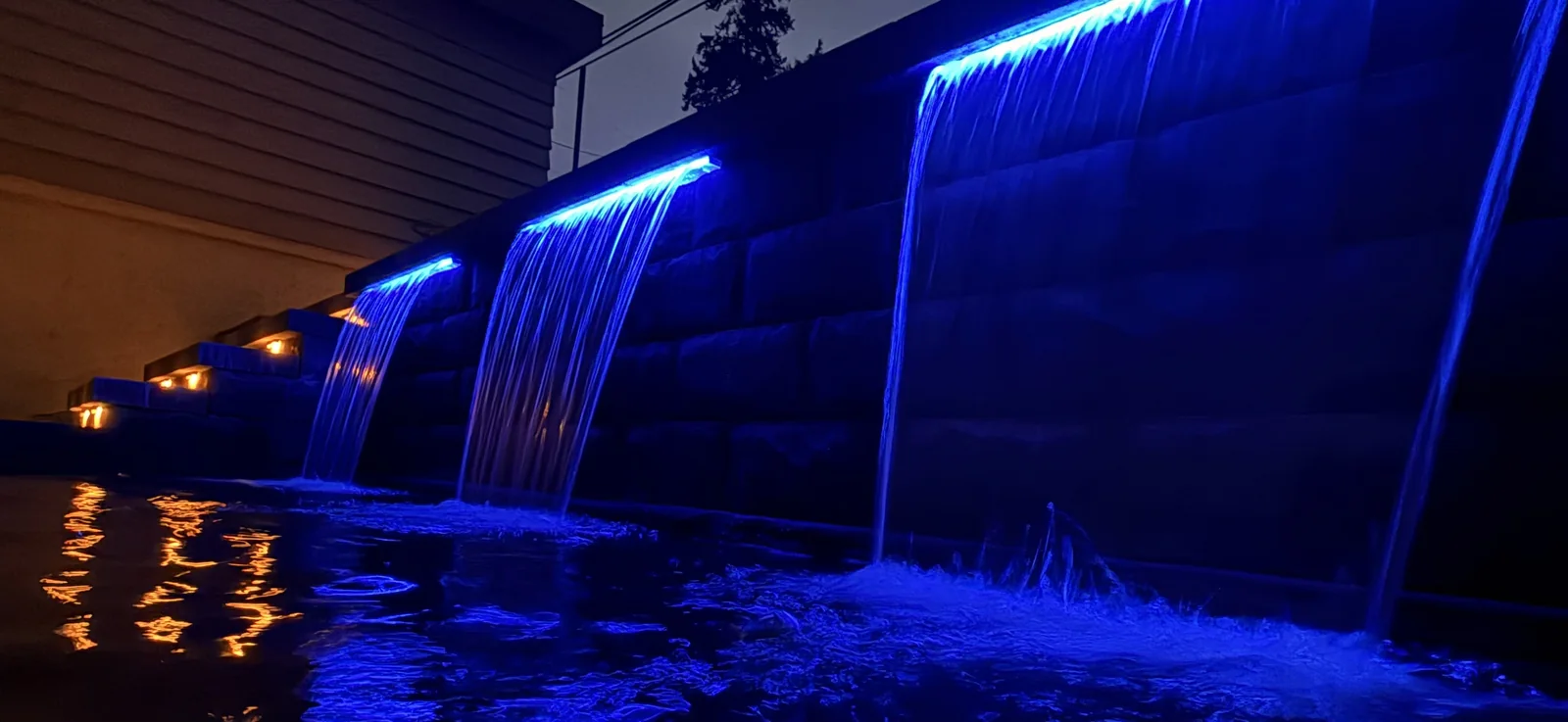 Three sheet waterfalls lit blue against a block wall at night