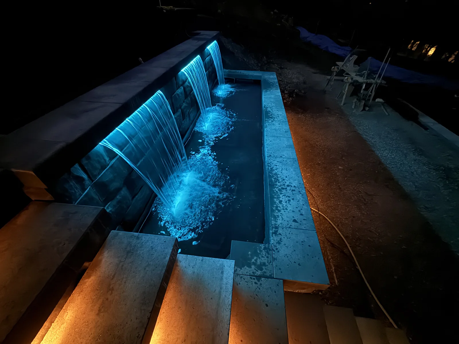Three water features in teal light pouring into the basin