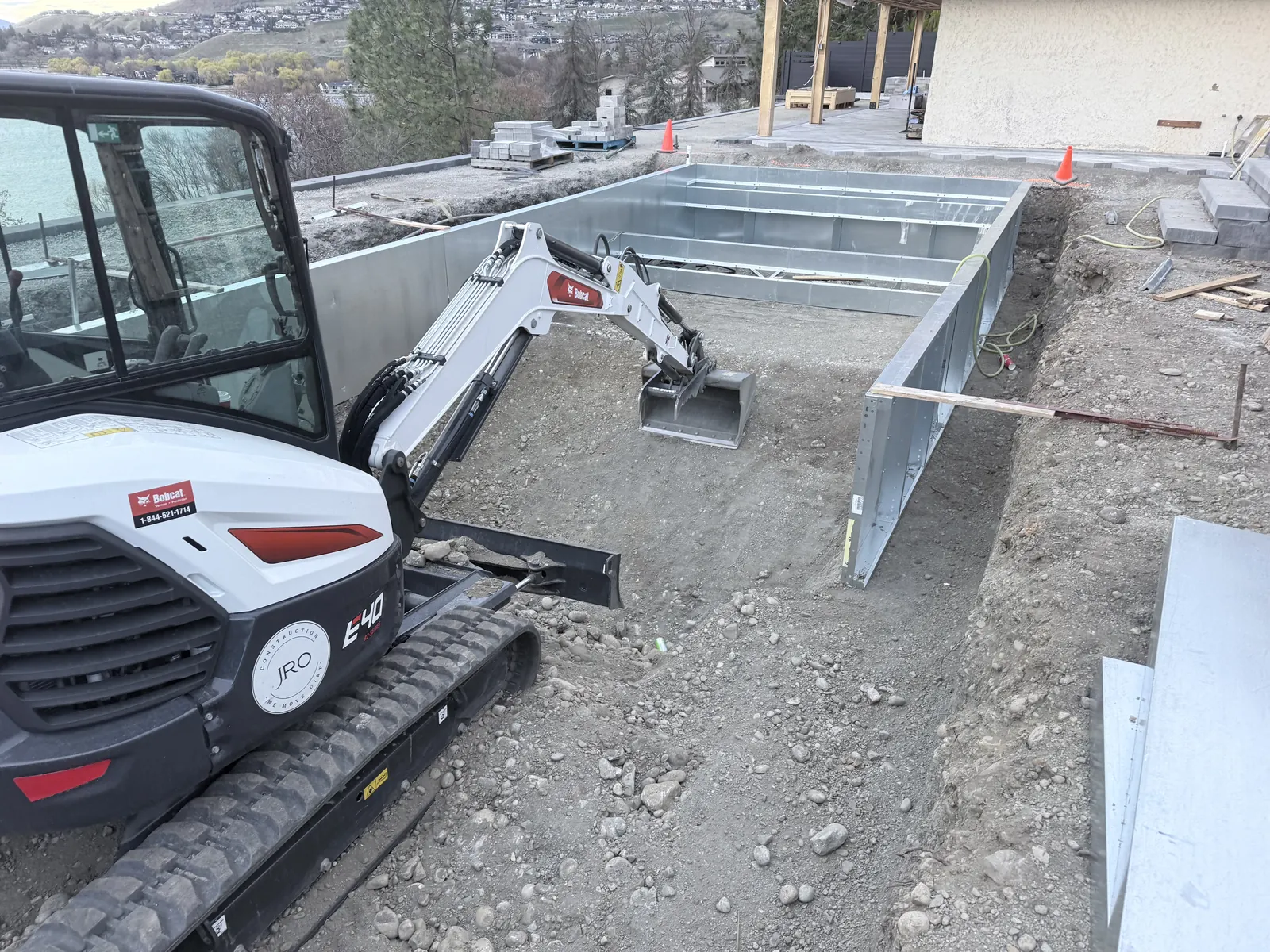 Pool walls set in the excavation with a mini excavator on site
