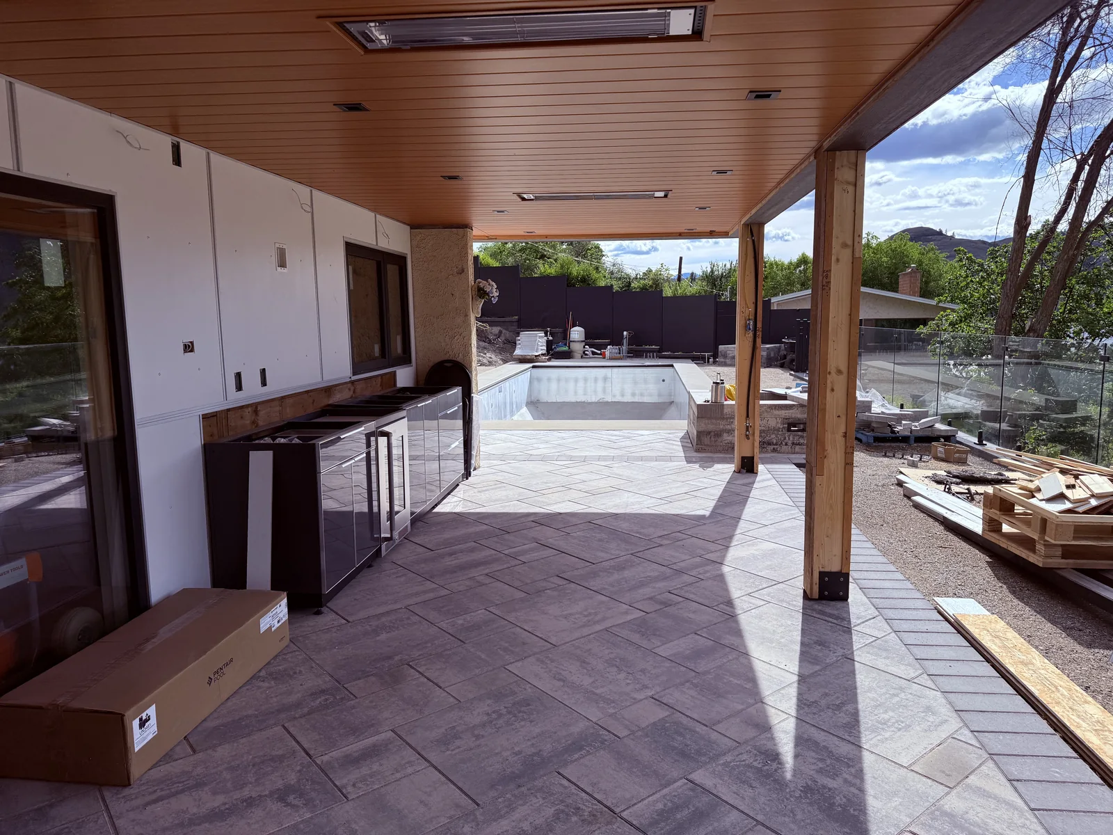 Covered outdoor kitchen patio with the pool and glass railing beyond
