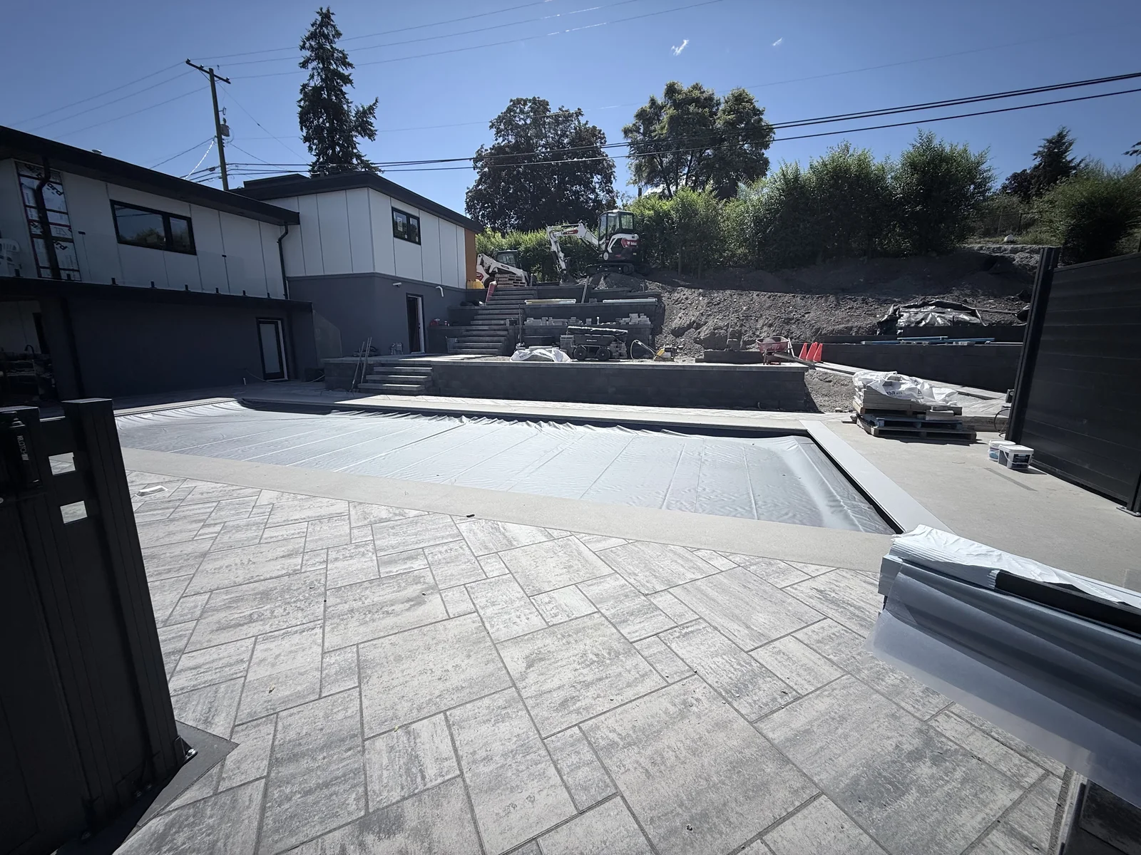 Covered pool beside the paver deck with the terraced hillside behind