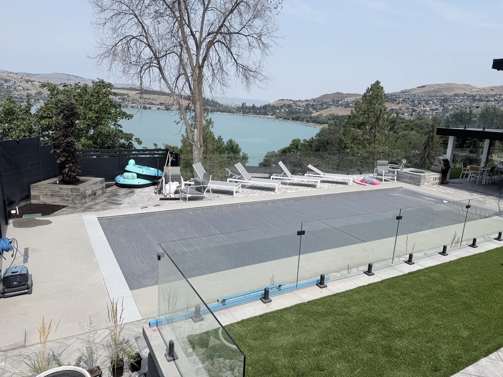 Pool deck with frameless glass railing, artificial turf and a lake view