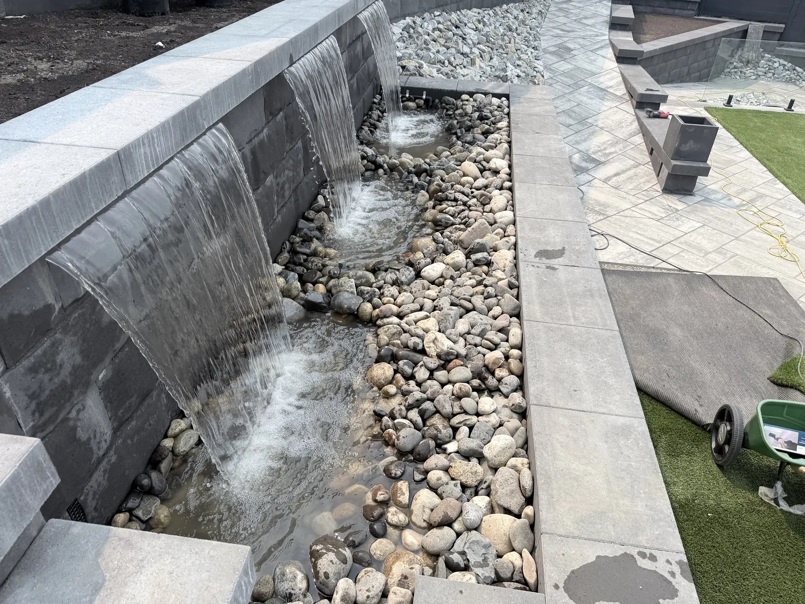 Water feature wall pouring into a river rock basin next to turf