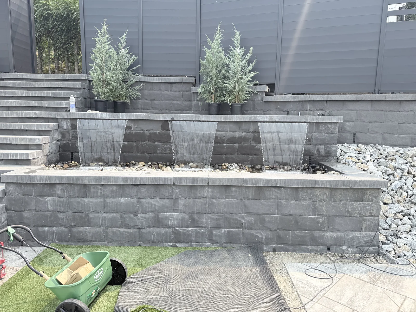Raised block wall with three water features and planted cedars above