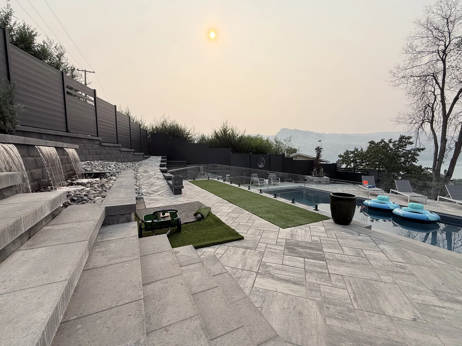 Finished pool deck with wide paver steps, turf strips and water feature walls