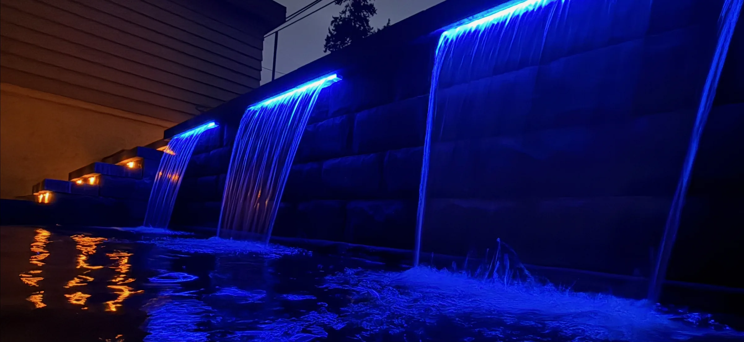 Illuminated water feature wall built into a terraced retaining wall at night